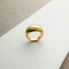 Gold dome ring on a white surface with a beige fabric background