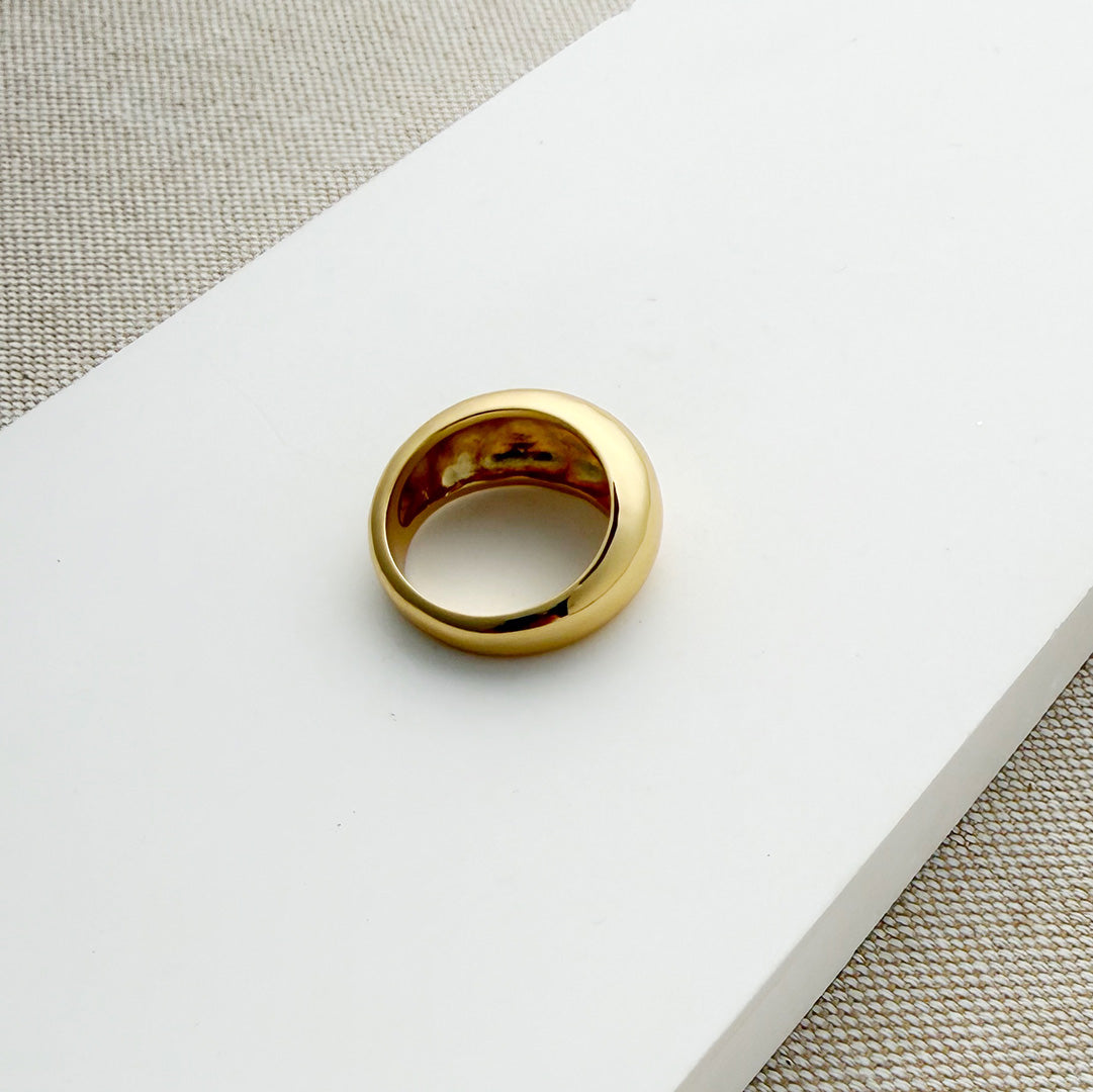 Gold dome ring on a white surface with a beige fabric background