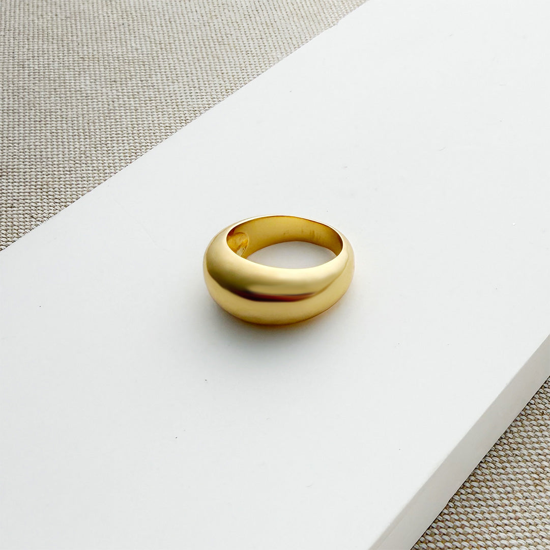 Gold dome ring on a white surface with a beige fabric background