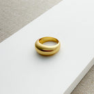 Gold dome ring on a white surface with a beige fabric background