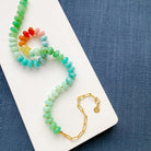 Necklace with multicolored gemstone beads on a white surface with blue fabric background