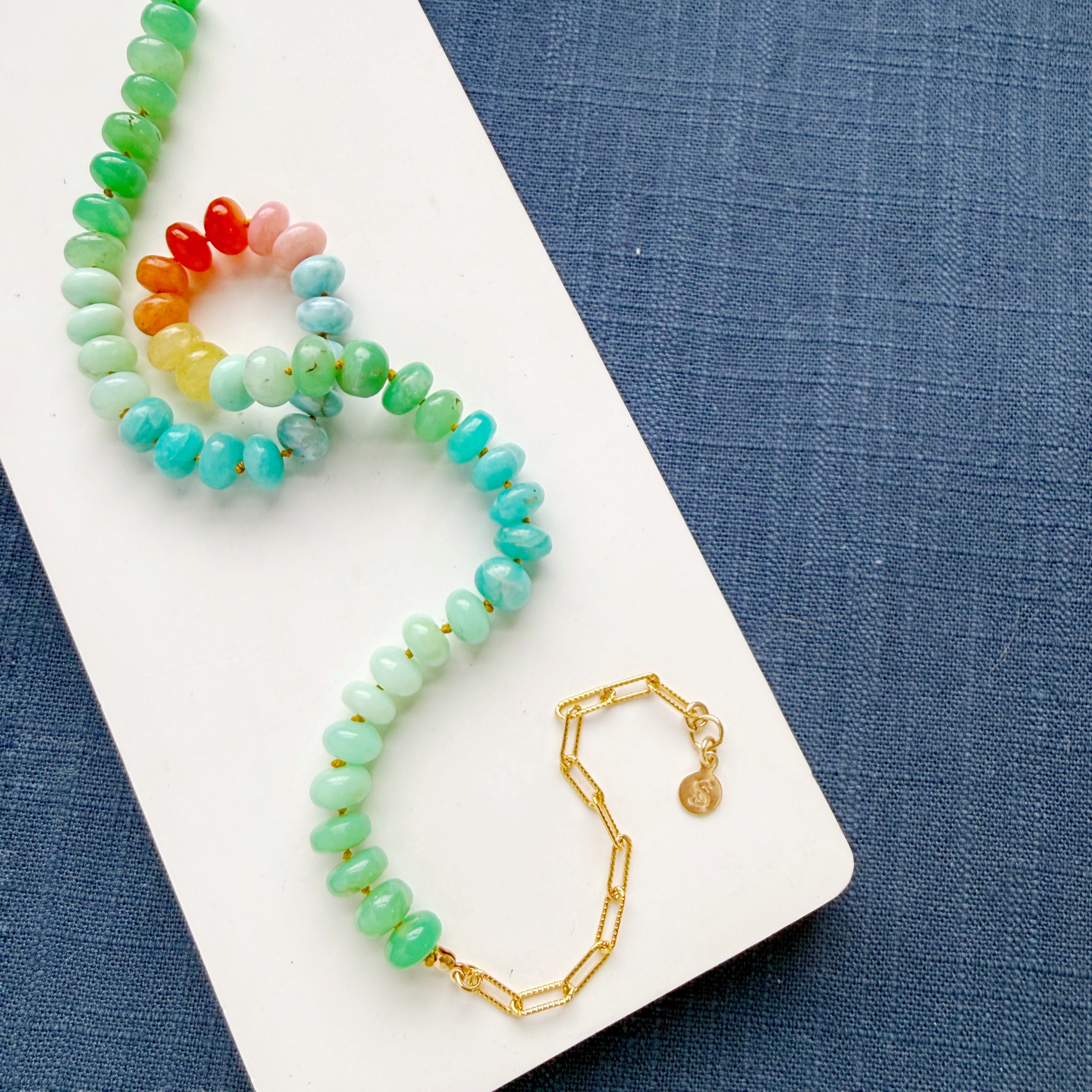 Necklace with multicolored gemstone beads on a white surface with blue fabric background