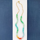 Necklace with multicolored gemstone beads on a white surface with blue fabric background
