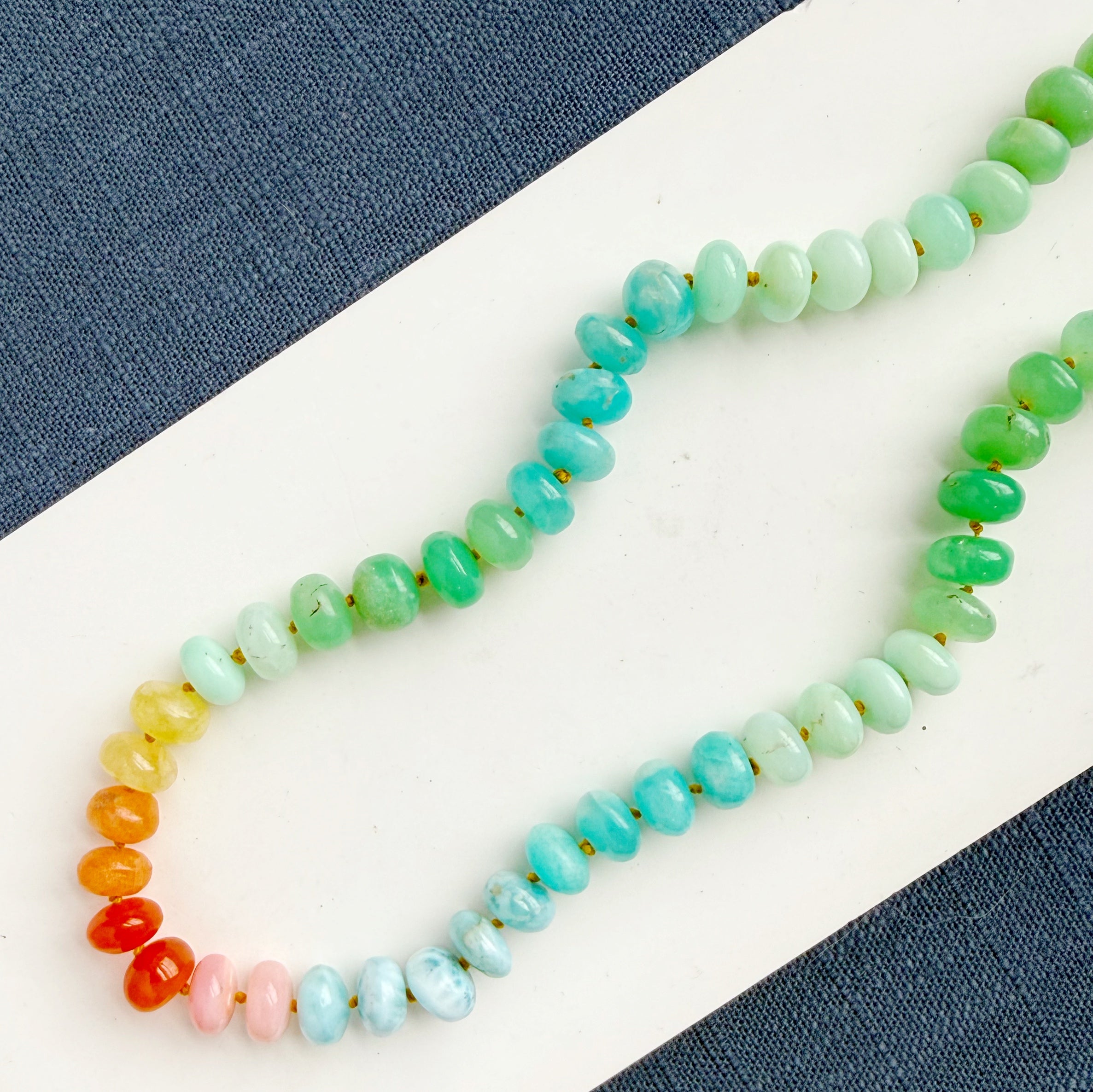 Necklace with multicolored gemstone beads on a white surface with blue fabric background