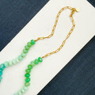Necklace with multicolored gemstone beads on a white surface with blue fabric background
