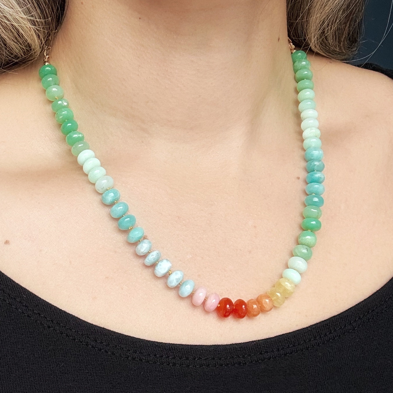 Necklace with multicolored gemstone beads worn by a person against a dark background