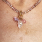 A close-up of a beaded necklace worn on a person's neck, featuring faceted pink and clear beads with a gold-tone clasp and three dangling charms, including a leaf-shaped crystal and oval pink beads.