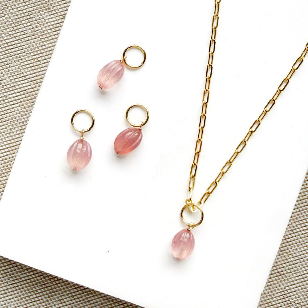 Carved pink chalcedony oval charm on a gold chain with a white card background