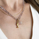 A close-up of a model wearing an ametrine gemstone necklace with a gold fish charm, carved pink chalcedony charm, and carved rose quartz charm