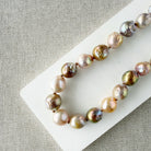 Champagne and rose baroque pearl necklace on a white dish and textured beige background