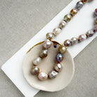 Champagne and rose baroque pearl necklace on a white dish and textured beige background