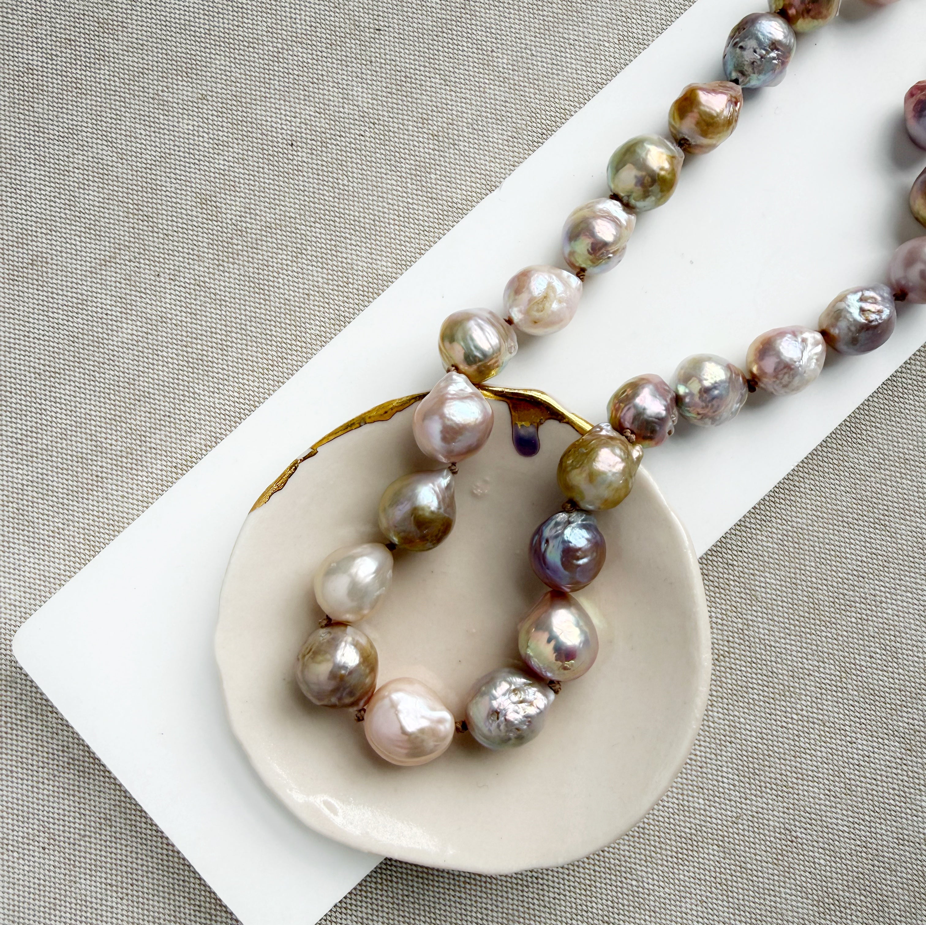 Champagne and rose baroque pearl necklace on a white dish and textured beige background
