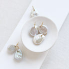 Keshi pearl charm with large gold ring in a white dish.