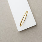 Gold bangle bracelet on a white card with a beige background
