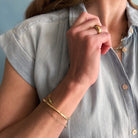 Person wearing gold jewelry including a ring and bracelets, with a light blue shirt.