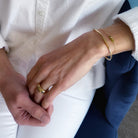 Close-up of two hands holding each other, wearing gold rings and bracelets.