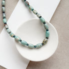 Necklace with teal agate beads on a white dish against a beige background