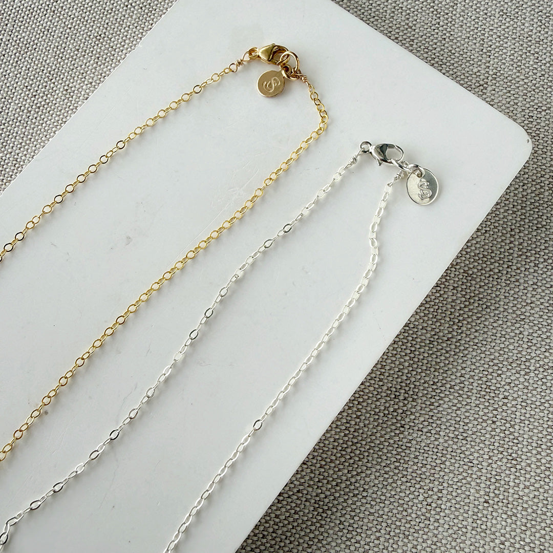 Clasp detail for gold and silver chain necklaces on a white card with a gray background