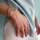 Hand wearing gold bracelets and a ring with a light blue and white background