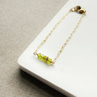 Gold bracelet with green beads on a white surface