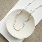 Pearl necklace on a white dish with a beige background