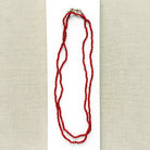 A long knotted necklace made of small red coral beads placed on a white rectangular display card over a textured light gray fabric background.