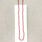 A long knotted necklace made of small red coral beads placed on a white rectangular display card over a textured light gray fabric background.
