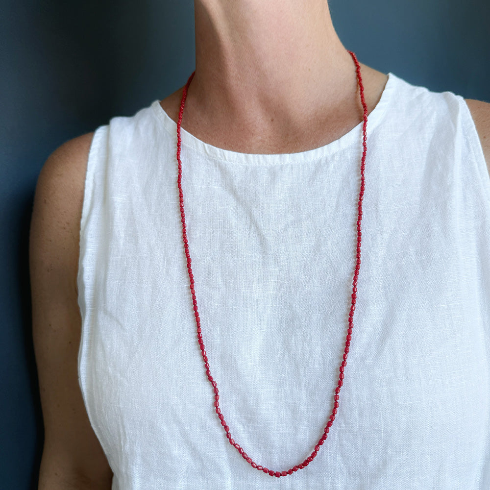 Woman wearing white tank with a long knotted necklace made of small coral beads
