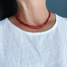 Woman wearing white tank with a long knotted necklace made of small coral beads