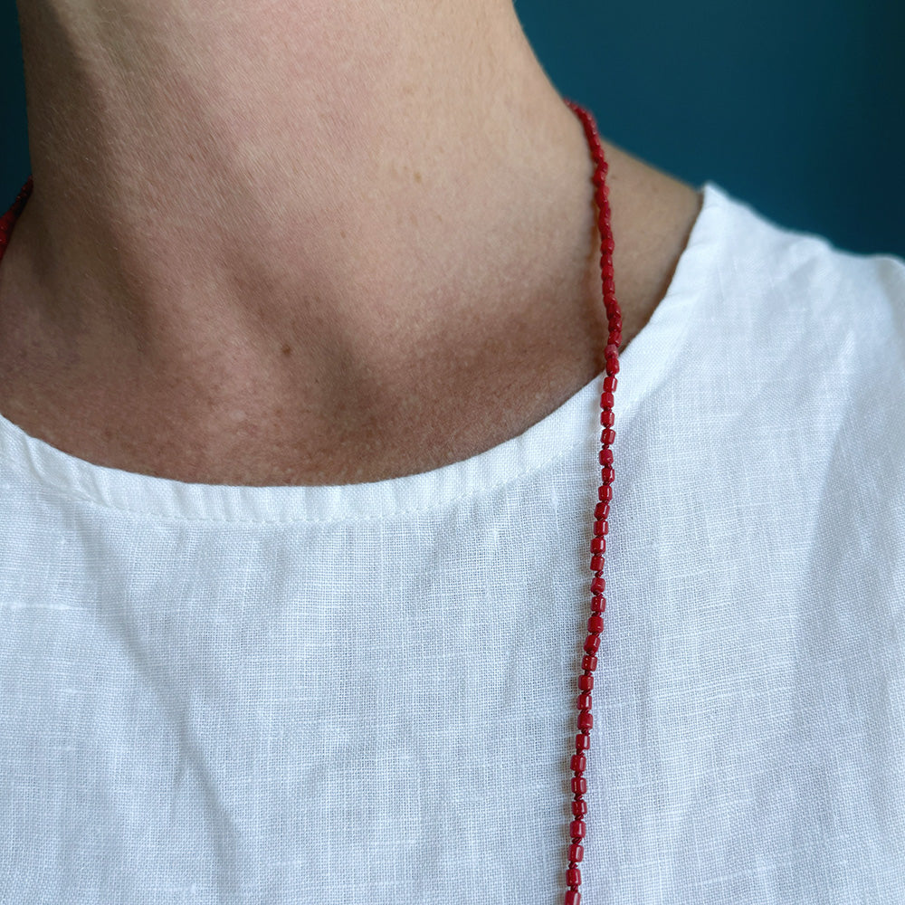 Woman wearing white tank with a long knotted necklace made of small coral beads