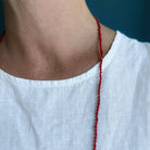 Woman wearing white tank with a long knotted necklace made of small coral beads