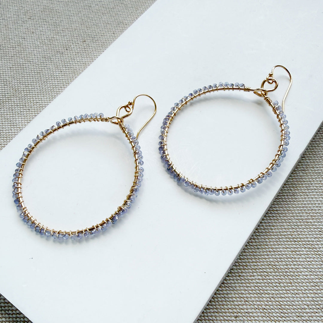 Large hoop earring hand wire wrapped in small tanzanite stones on a white background