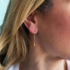 Close-up of a person wearing a gold teardrop earring with green and blue gemstones.