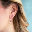 Close-up of an ear wearing a gold teardrop earring with gesmtones against a light blue background