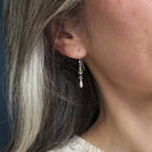 Close-up of a person wearing a silver teardrop earring with green and blue gemstones.