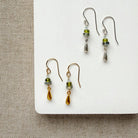 Dainty teardrop and gemstone earrings in gold and silver on a white plate.