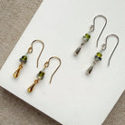 Dainty teardrop and gemstone earrings in gold and silver on a white plate.