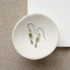 Pair of silver earrings with green and blue gemstones on a white dish.
