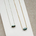Two necklaces, one silver and one gold, with a single labradorite gemstone on a white dish against a textured surface