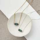 Two necklaces, one silver and one gold, with a single labradorite gemstone on a white dish against a textured surface