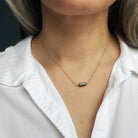 Necklace with a labradorite gemstone worn by a person in a white shirt against a dark background