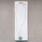 Round chalcedony pendant on a gold chain on a white card