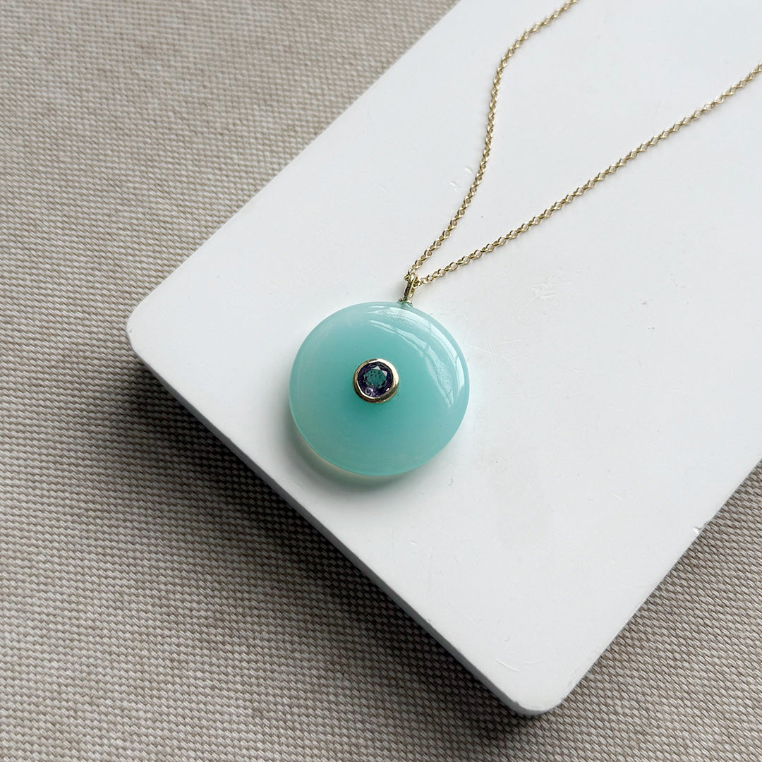 Round chalcedony pendant on a gold chain on a white card