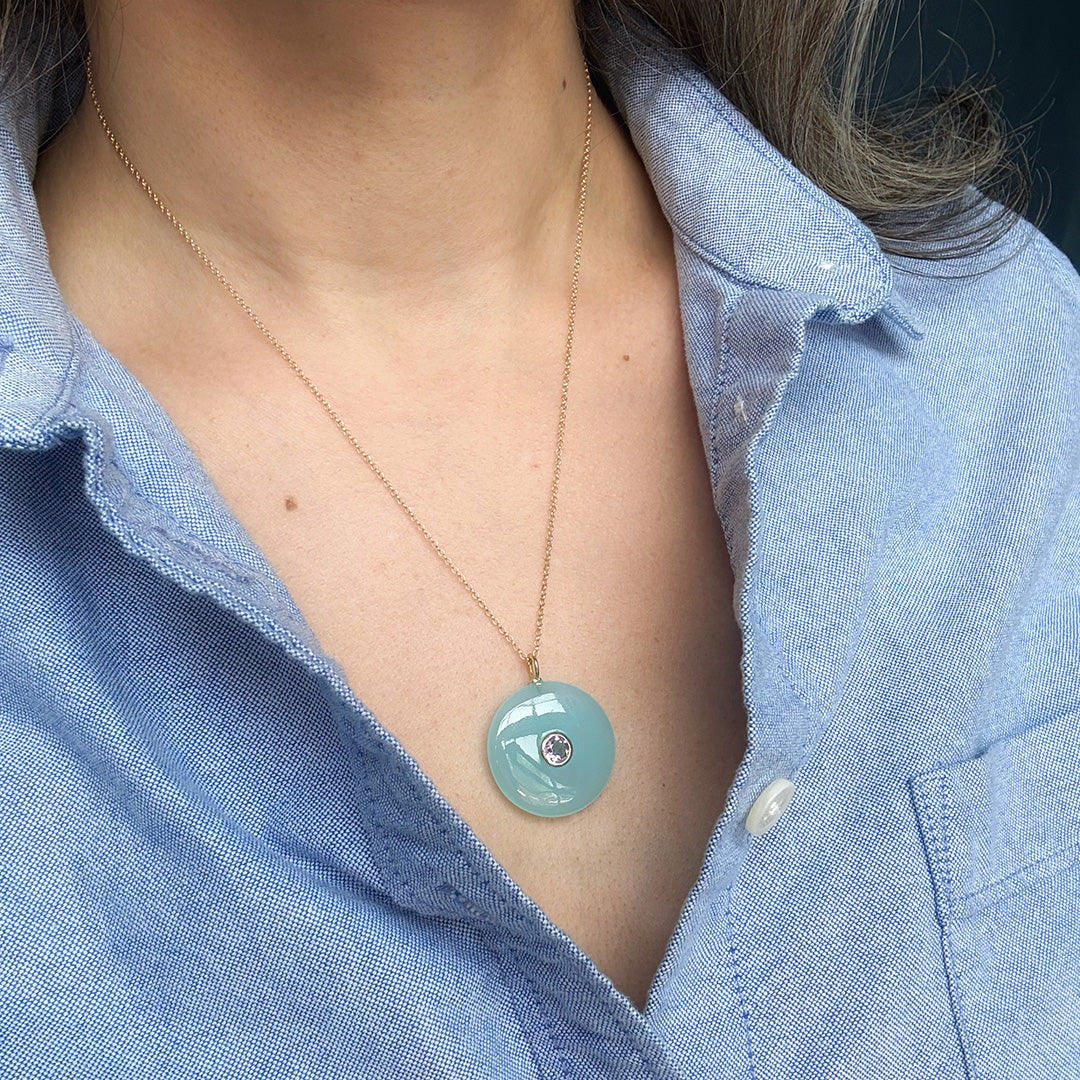 Close up of woman wearing a round chalcedony pendant on a gold chain 