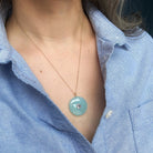 Close up of woman wearing a round chalcedony pendant on a gold chain 