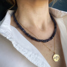 Close up of woman wearing a gemstone necklace layered with a gold elephant pendant necklace