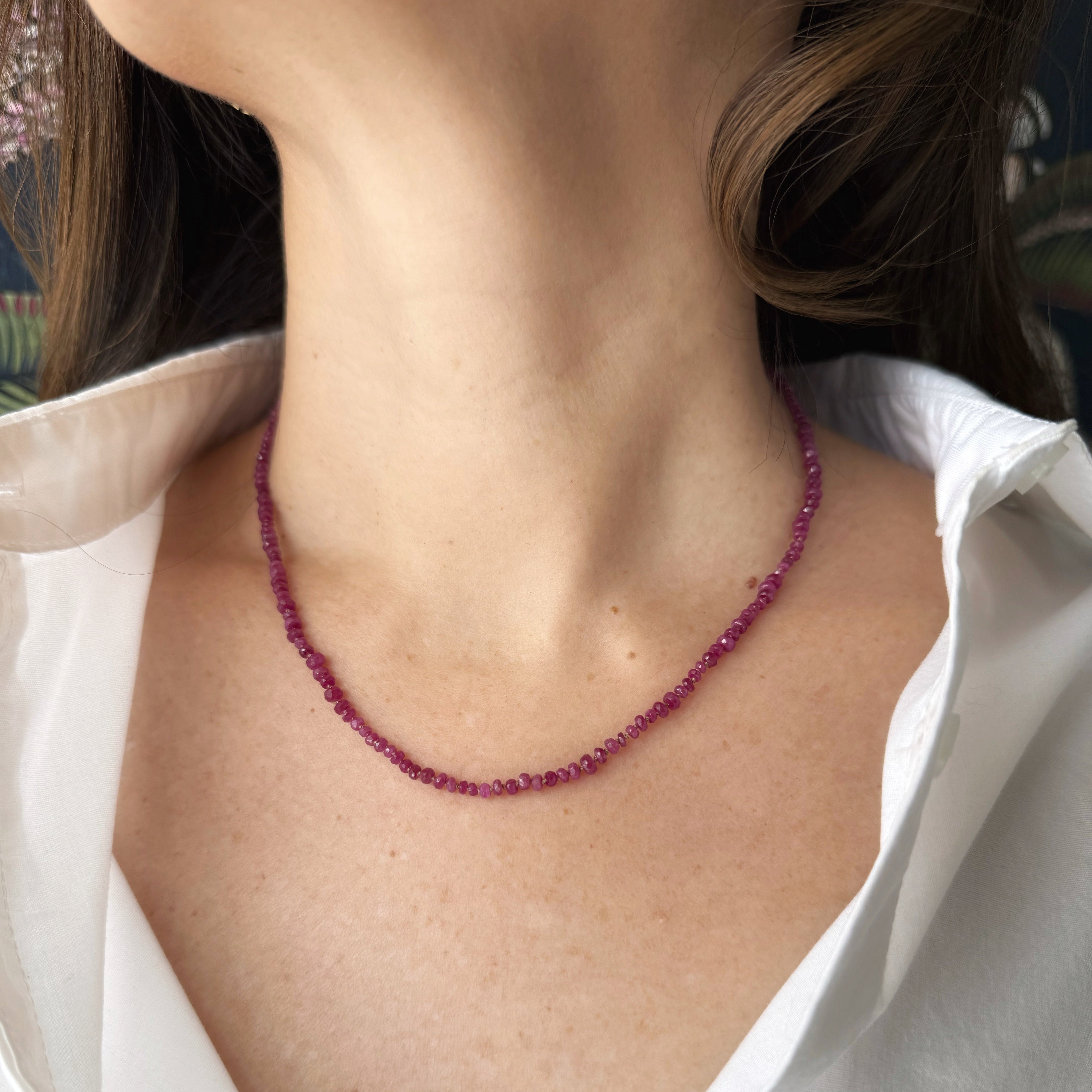 Ruby gem necklace worn by a person in a white shirt.