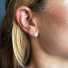 A close-up of a person's ear wearing a small round gold stud earring with a pave diamonds.