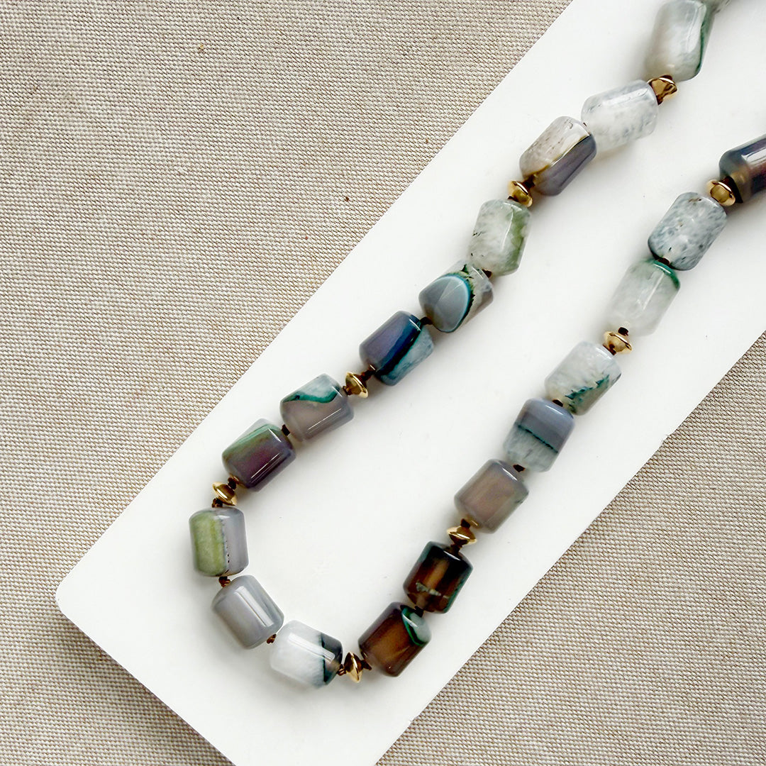 Necklace with multicolored beads on a white tray against a beige fabric background