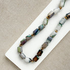 Necklace with multicolored beads on a white tray against a beige fabric background